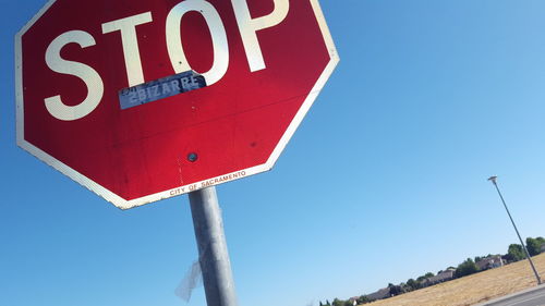 Low angle view of road sign against clear blue sky