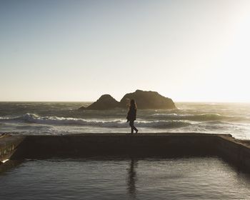 Woman walking by sea against sky