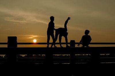 Silhouette male friends on railing against orange sky