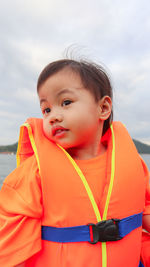 Cute baby girl wearing life jacket on boat against sky
