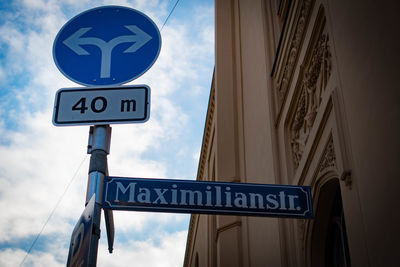 Low angle view of road sign by building against cloudy sky