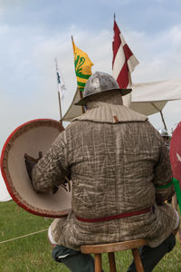 Rear view of man wearing traditional clothing sitting on stool against sky