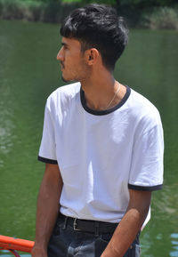 A south asian guy wearing white t-shirt and black jeans, posing by lake and looking sideways 