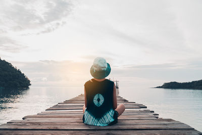Man sitting on pier over lake against sky