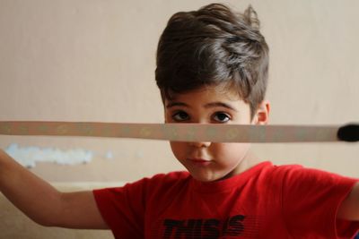 Close-up portrait of boy holding ribbon against wall