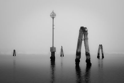 Wooden posts in sea against sky