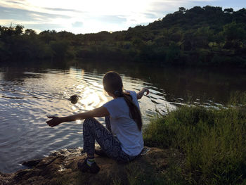 Rear view of woman sitting by lake against sky