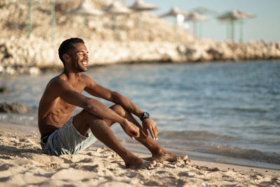 Side view of young man sitting at beach