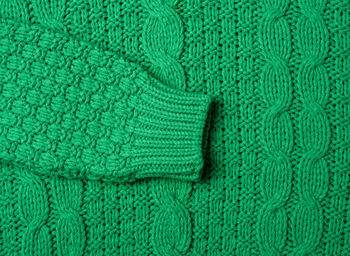 Chunky knit of a sweater with green threads, full frame. cozy and warm clothes