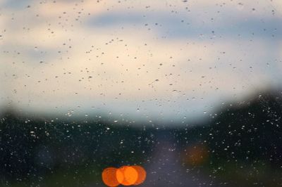 Close-up of raindrops on window against sky during rainy season