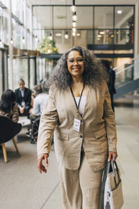 Portrait of happy mature businesswoman walking with purse at convention center