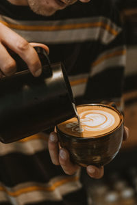 Cropped hand of man pouring latte art