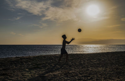 Silhouette person playing with ball on beach against sky during sunset