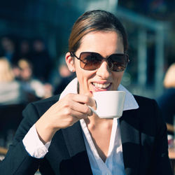 Smiling businesswoman drinking coffee while sitting at sidewalk cafe