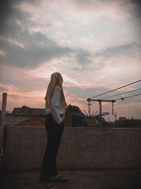 Rear view of woman standing against sky during sunset