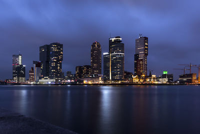 Illuminated buildings by river against sky at night