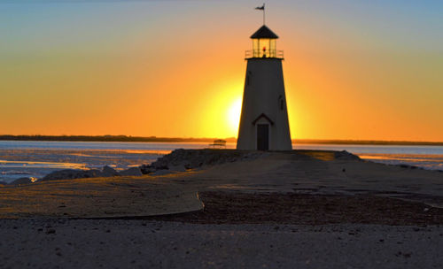 Lighthouse by sea against sky during sunset