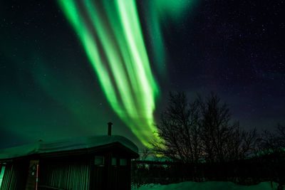 Low angle view of snow covered house during aurora borealis