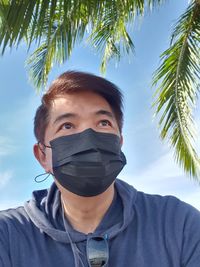 Portrait of young man with palm trees against sky