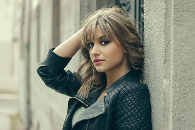 Portrait of confident young woman standing against wall