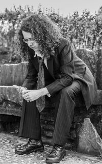 Thoughtful young woman wearing suit sitting on rock at park