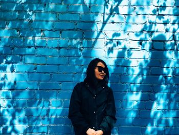 Woman wearing sunglasses standing against blue wall