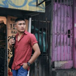 Portrait of young man looking away while standing against building