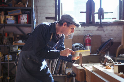 Carpenter cutting wood with handsaw in workshop