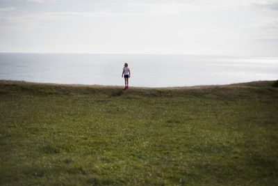 Woman standing on field by sea against sky