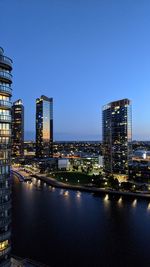 Illuminated buildings by river against blue sky