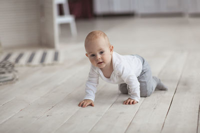 Baby of 10 months in light clothes is crawling on a wooden floor, a light real interior.