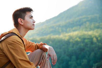 Side view of young man looking away against mountain