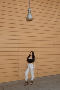 Full length of fashionable young woman standing against wall