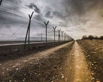 Fence on field against storm clouds