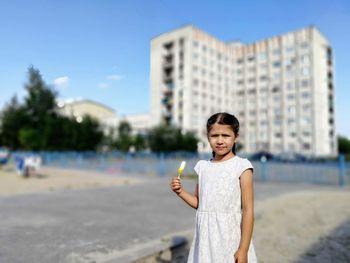 Portrait of cute girl holding flavored ice while standing in city