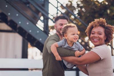 Black mom and white dad holding baby boy and playing airplane