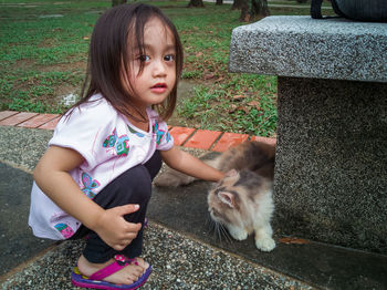 Portrait of cute girl crouching by cat at park