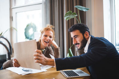 Smiling female illustrator showing drawing to male entrepreneur at office