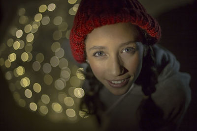 High angle portrait of smiling teenage girl wearing warm clothing standing against illuminated lights