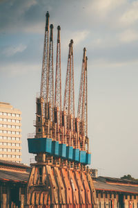 Low angle view of crane by building against sky