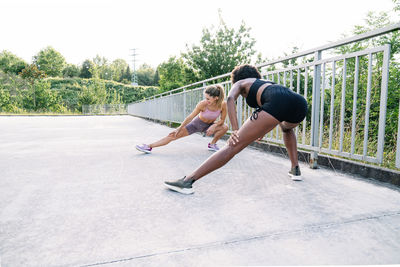 Multiracial fit female friends in sportswear doing side lunges while warming up and stretching legs before workout