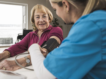 Home caregiver examining blood pressure of smiling woman with machine