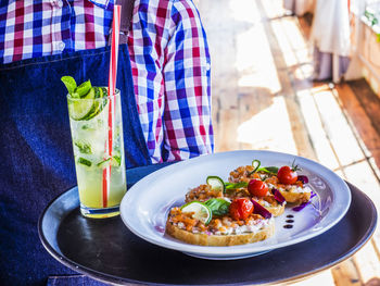 Midsection of waitress carrying tray with open faced sandwiches and lemonade at restaurant