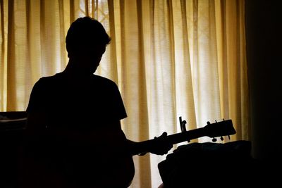 Rear view of man playing guitar at home