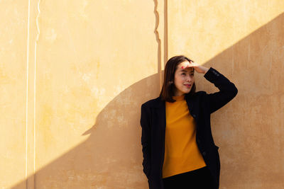 Woman shielding eyes while standing against wall