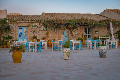 Empty chairs and tables outside house against blue sky