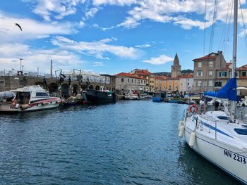 Sailboats moored on harbor by buildings in city against sky