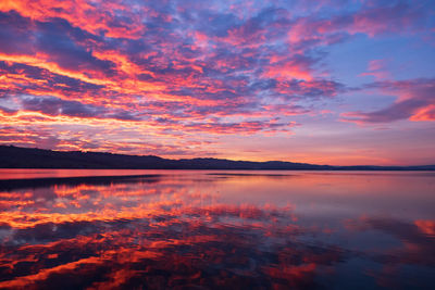 Scenic view of lake against dramatic sky during sunset