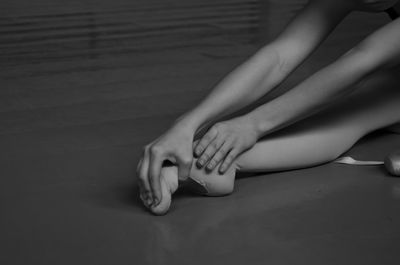 Low section of ballet dancer stretching foot while sitting on floor