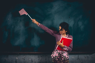 Woman holding umbrella standing against wall